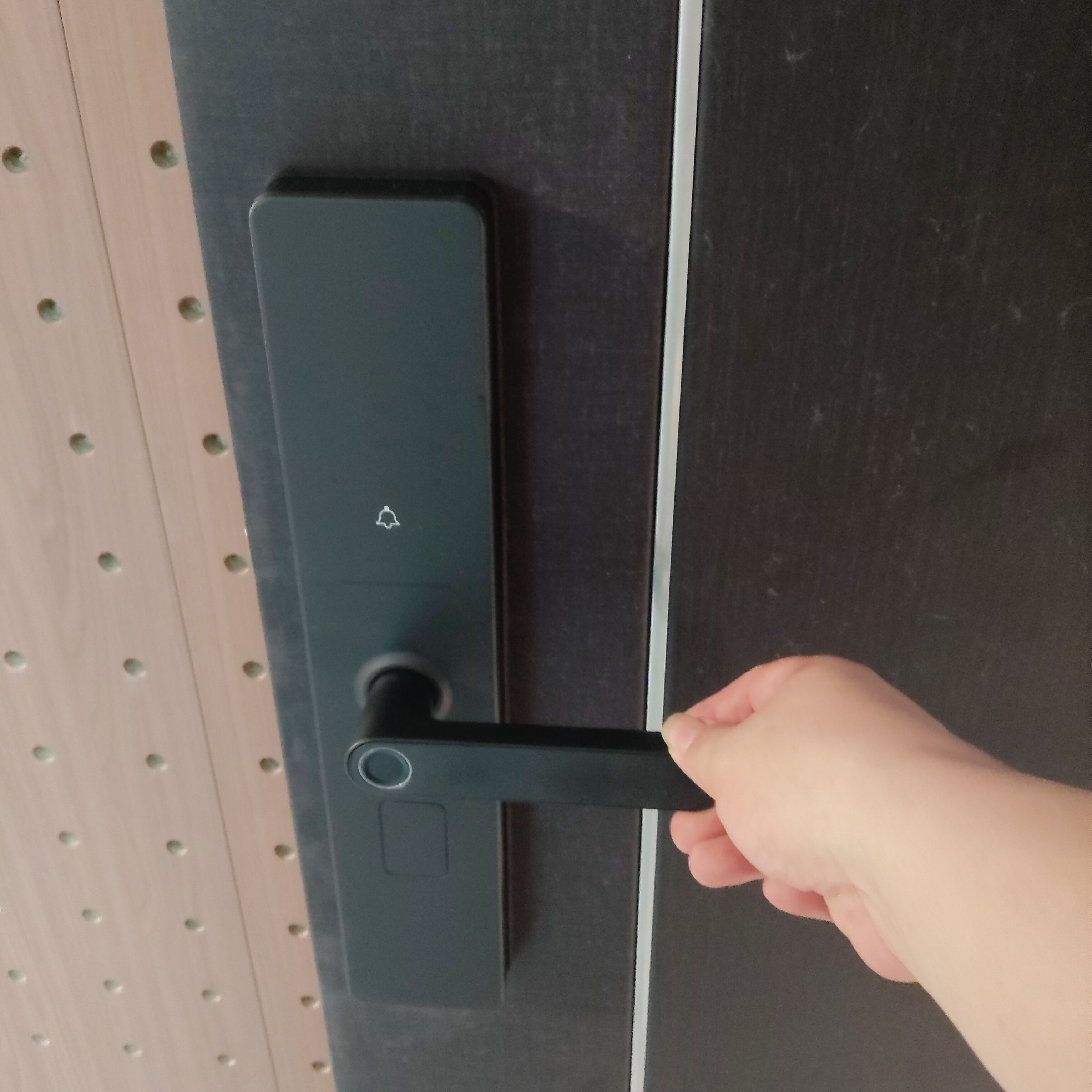 现代智能指纹锁产品展示,金属质感表面,多个按键区域,屏幕显示,安装在白色门上,背景为浅色墙面